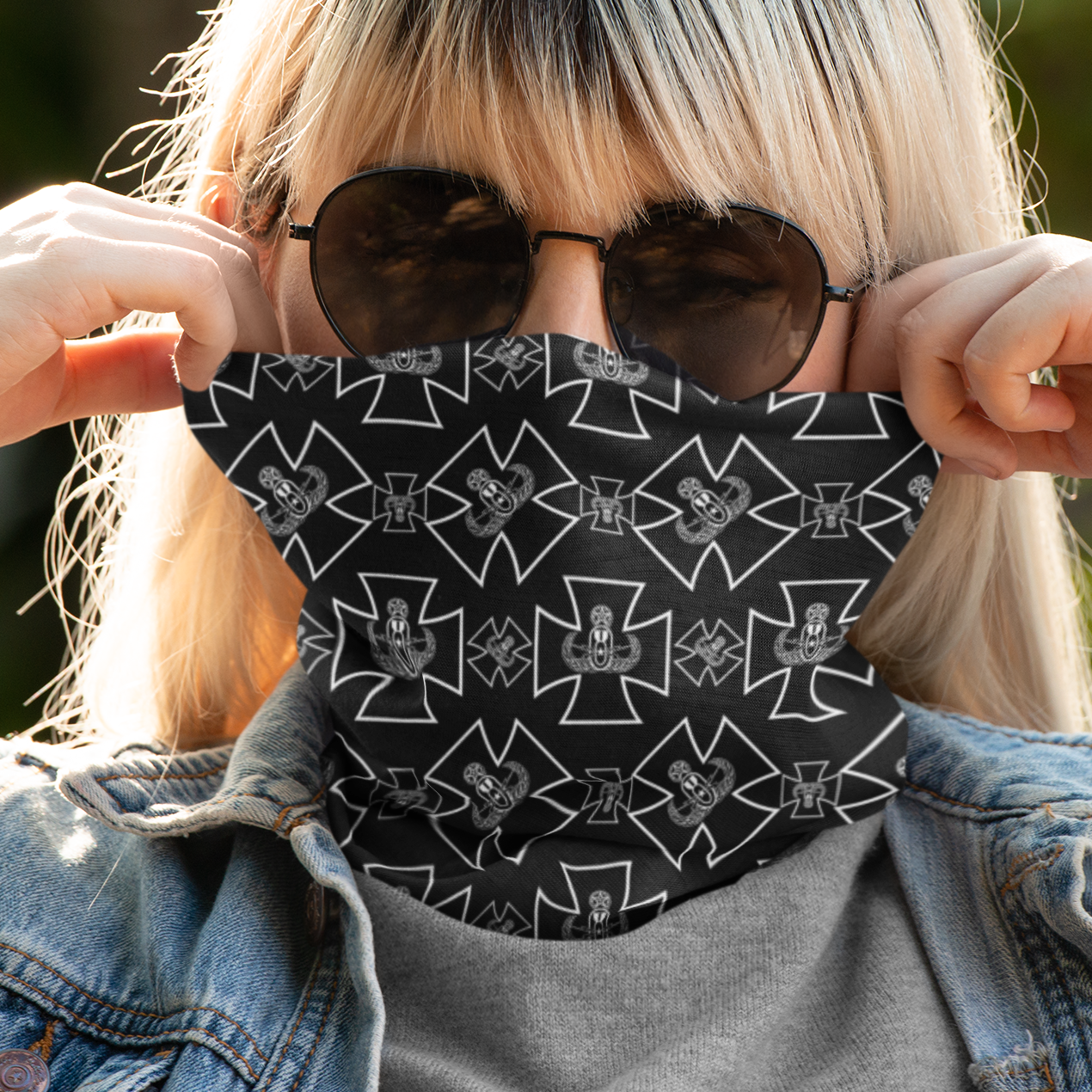 Person wearing a black patterned face mask and sunglasses with a denim jacket.