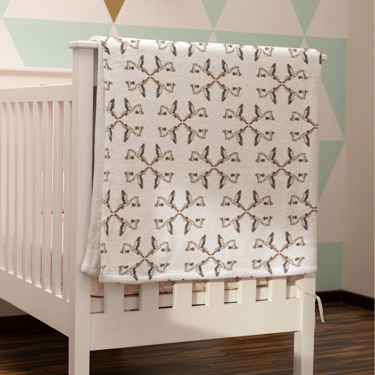 White crib with a patterned blanket against a geometric wall design.