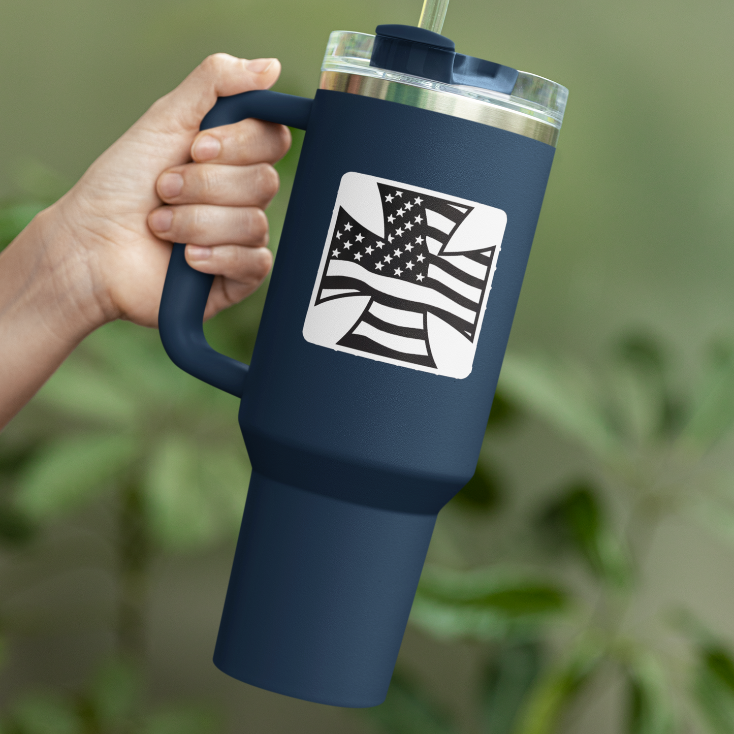 Navy blue tumbler with American flag design held by a hand against a blurred green background