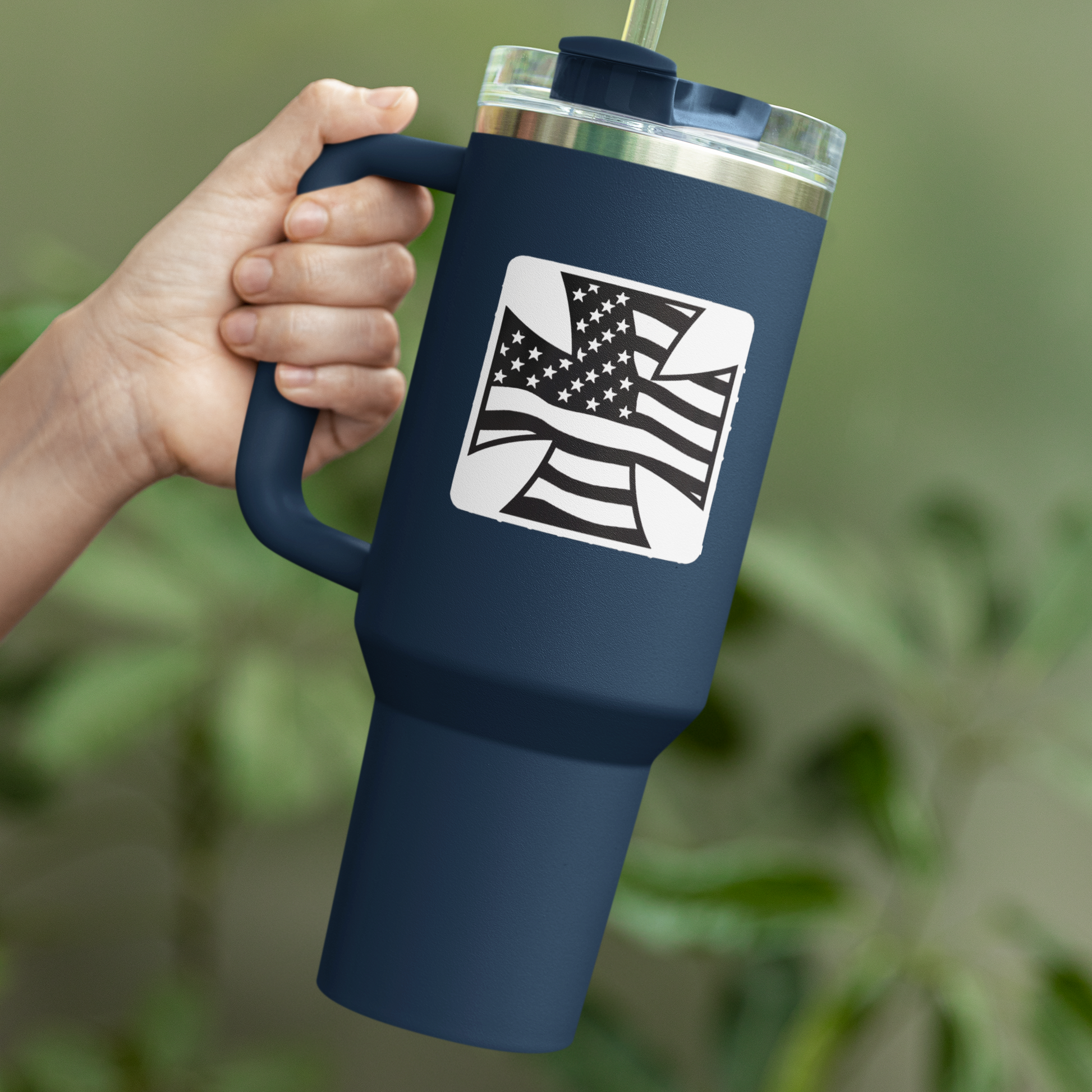 Navy blue tumbler with American flag design held by a hand against a blurred green background